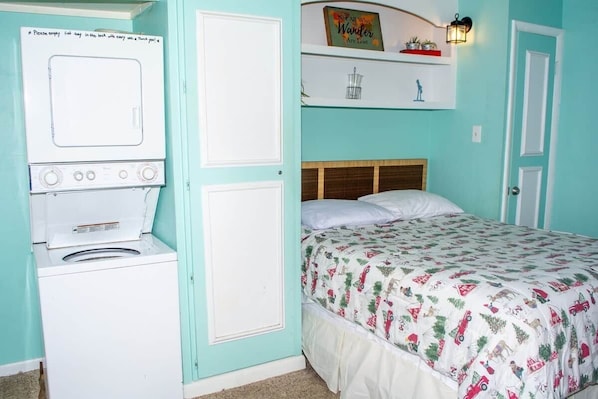 A bedroom with a bed, a washing machine, and a shelf with decorative items.