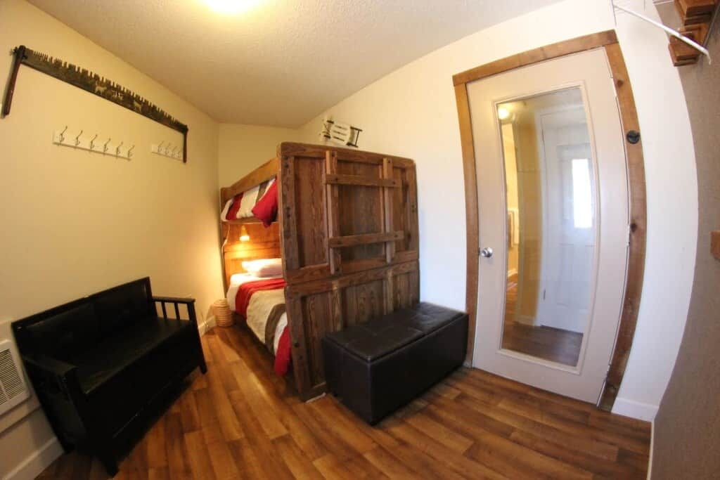 A room with a bunk bed, a bench, a coat rack, and a door with a mirror.
