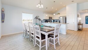 A spacious kitchen with white cabinets, a central island, and a dining area with a wooden table and white chairs. - Pet Friendly, Golf Cart Access, Boat Parking (Port Aransas)