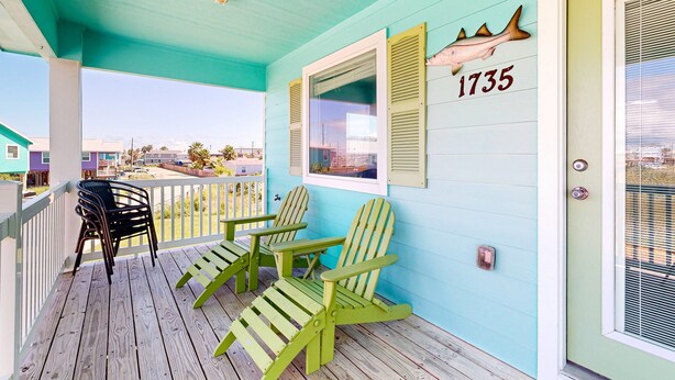 A porch with two green Adirondack chairs, a white railing, and a door with a number "1735" and a fish decoration. - Pet Friendly, Golf Cart Access, Boat Parking (Port Aransas)