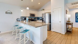 A modern kitchen with white cabinets, a granite island, and bar stools. - Pet Friendly, Golf Cart Access, Boat Parking (Port Aransas)