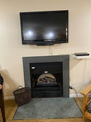 Ein Wohnzimmer mit Flachbildfernseher über einem Kamin, einem Korbwäsches und einem Holztisch.