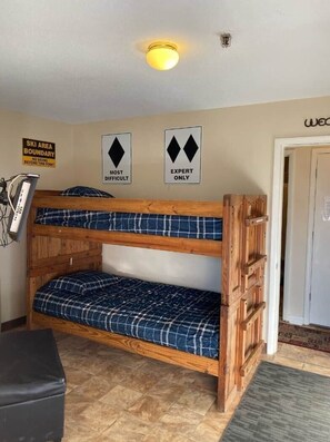 A bunk bed with a wooden frame and plaid bedding, a wall-mounted ski area boundary sign, and a door with a sign above it. - Winterplace D105 Ski in Ski out condo First Floor (Ghent)