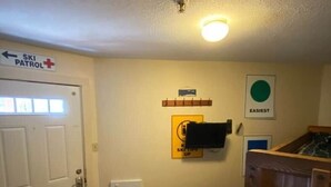 A hallway with a door marked 'SKI PATROL,' a wall-mounted heater, a wooden bench, and a framed picture labeled 'EASIEST.' - Winterplace D105 Ski in Ski out condo First Floor (Ghent)