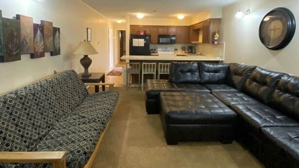 A living room with a sofa, ottoman, and a dining area with a kitchen in the background. - Winterplace D105 Ski in Ski out condo First Floor (Ghent)