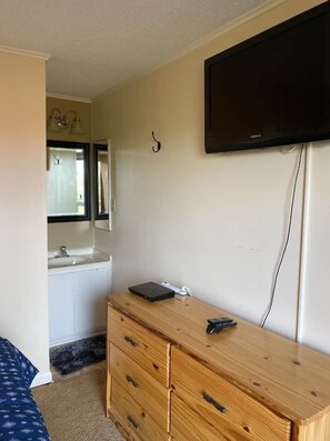 Een slaapkamer met een houten dressoir, een flatscreen televisie aan de muur, een spiegel boven het dressoir en een raam met gordijnen.