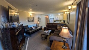 A compact living space with a sofa, a coffee table, a TV, and a kitchen area in the background.