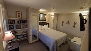 Une chambre à coucher comprenant un lit, une table de chevet, une lampe, une bibliothèque et un miroir.