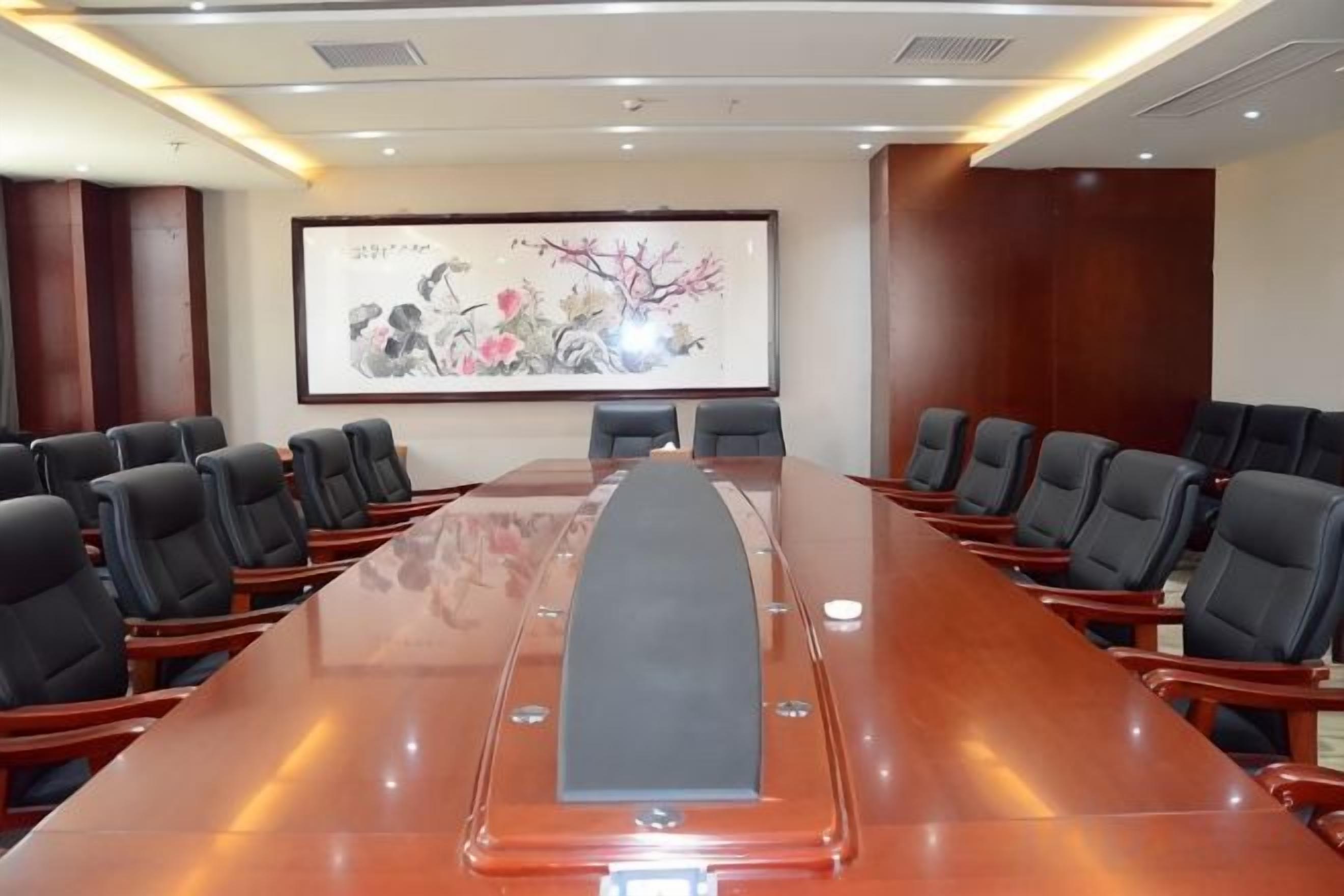 Un salón de conferencias con una larga mesa, sillas y una pantalla de proyector.