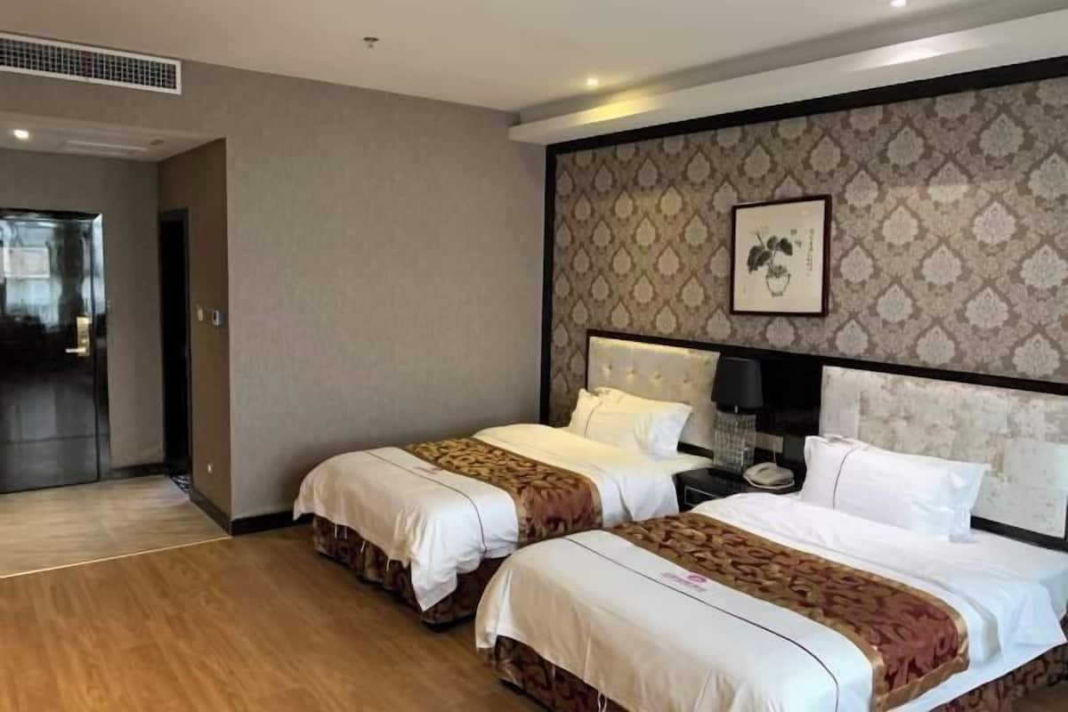 Een hotelkamer met twee bedden, een hoofdeinde met een patroon, een ingelijst schilderij aan de muur en een nachtkastje met een lamp.