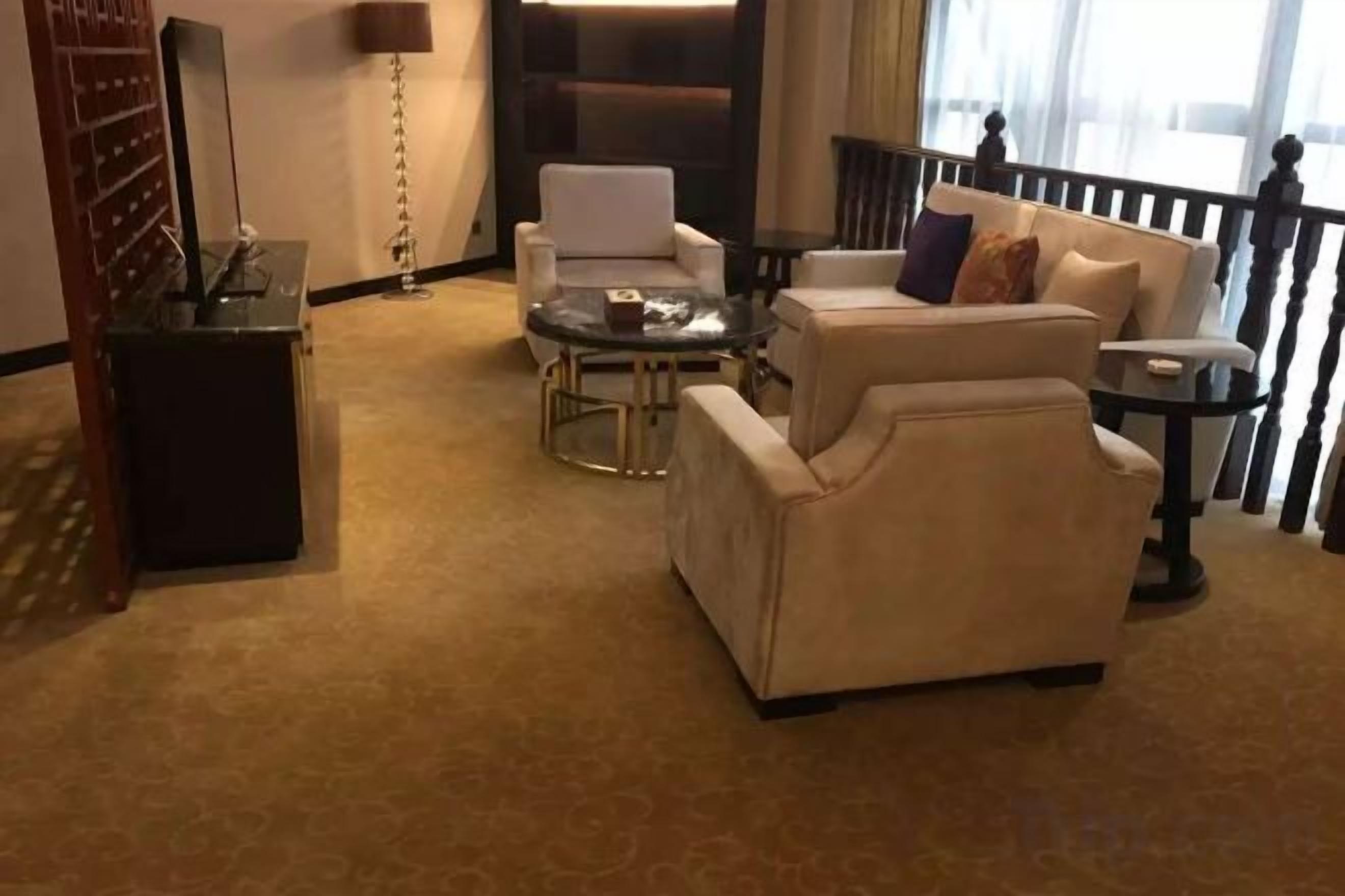 Quarto de hotel com sofá, poltrona e uma pequena mesa. Há uma luminária e um objeto decorativo na mesa.