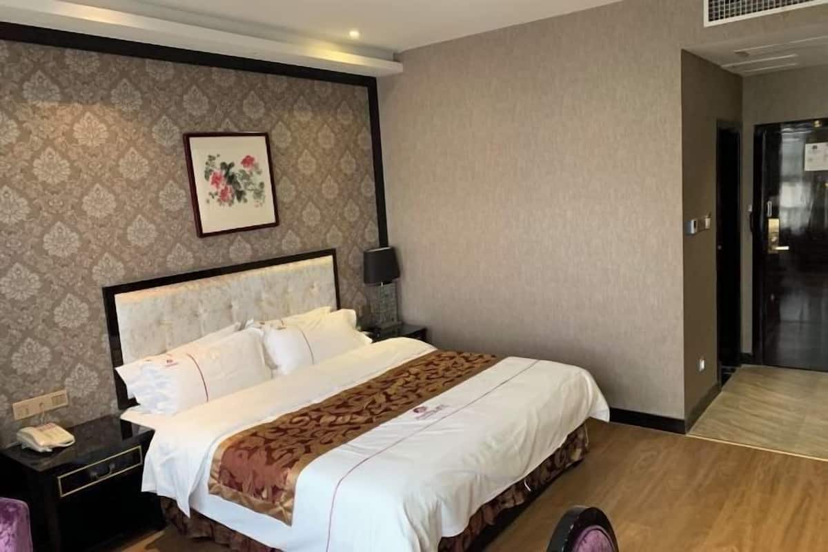 Een hotelkamer met een bed, nachtkastje, lamp en een ingelijst schilderij aan de muur.