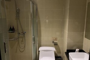 Une salle de bain avec une douche à parois de verre, des toilettes blanches et un lavabo noir.