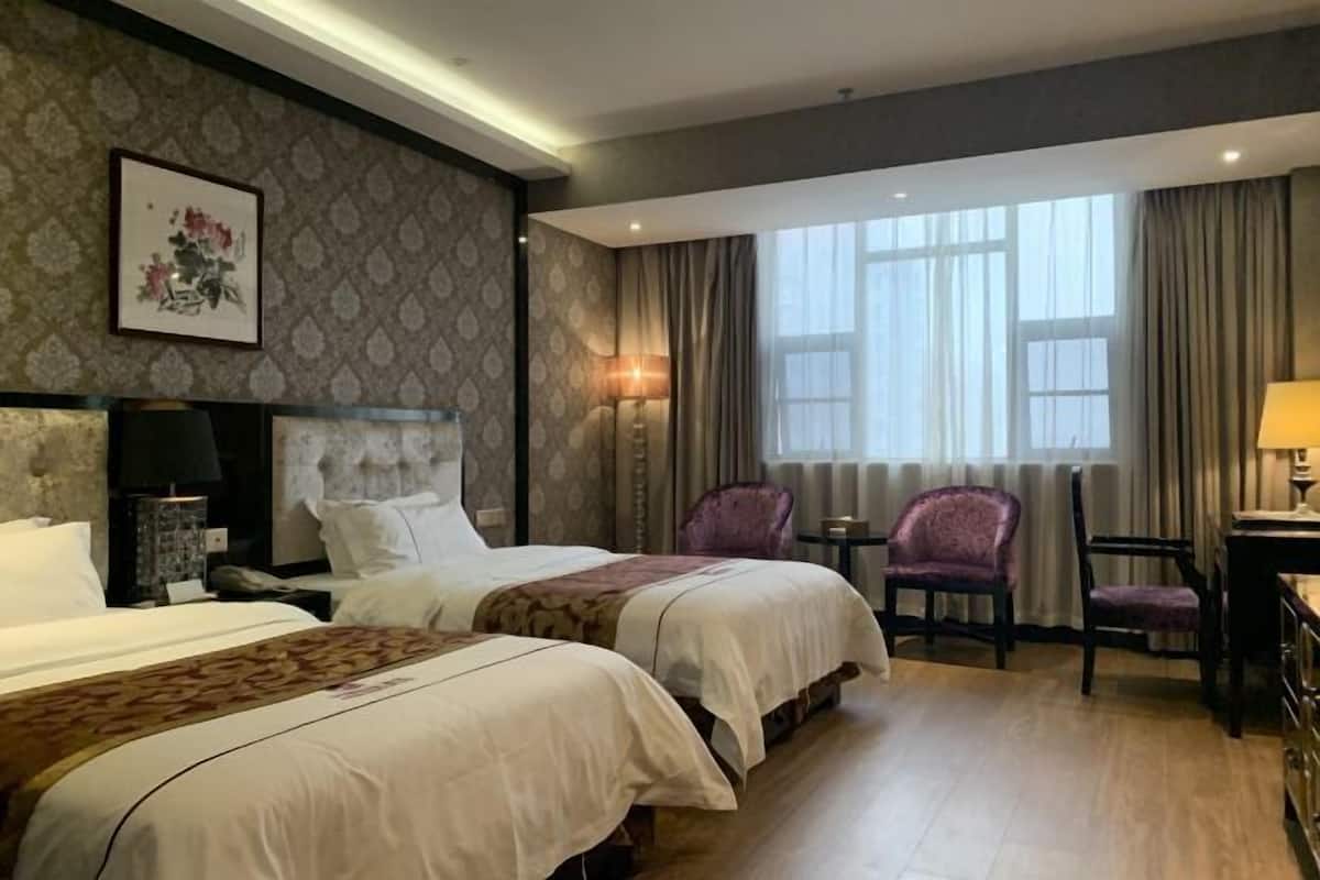 Een hotelkamer met twee bedden, een bureau, een stoel en een groot raam met gordijnen.