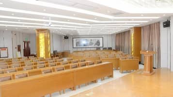 A conference room with rows of wooden chairs, a podium, and a large screen.