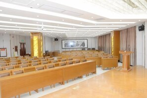 Un salón de conferencias con filas de sillas de madera, un atril y una pantalla grande.