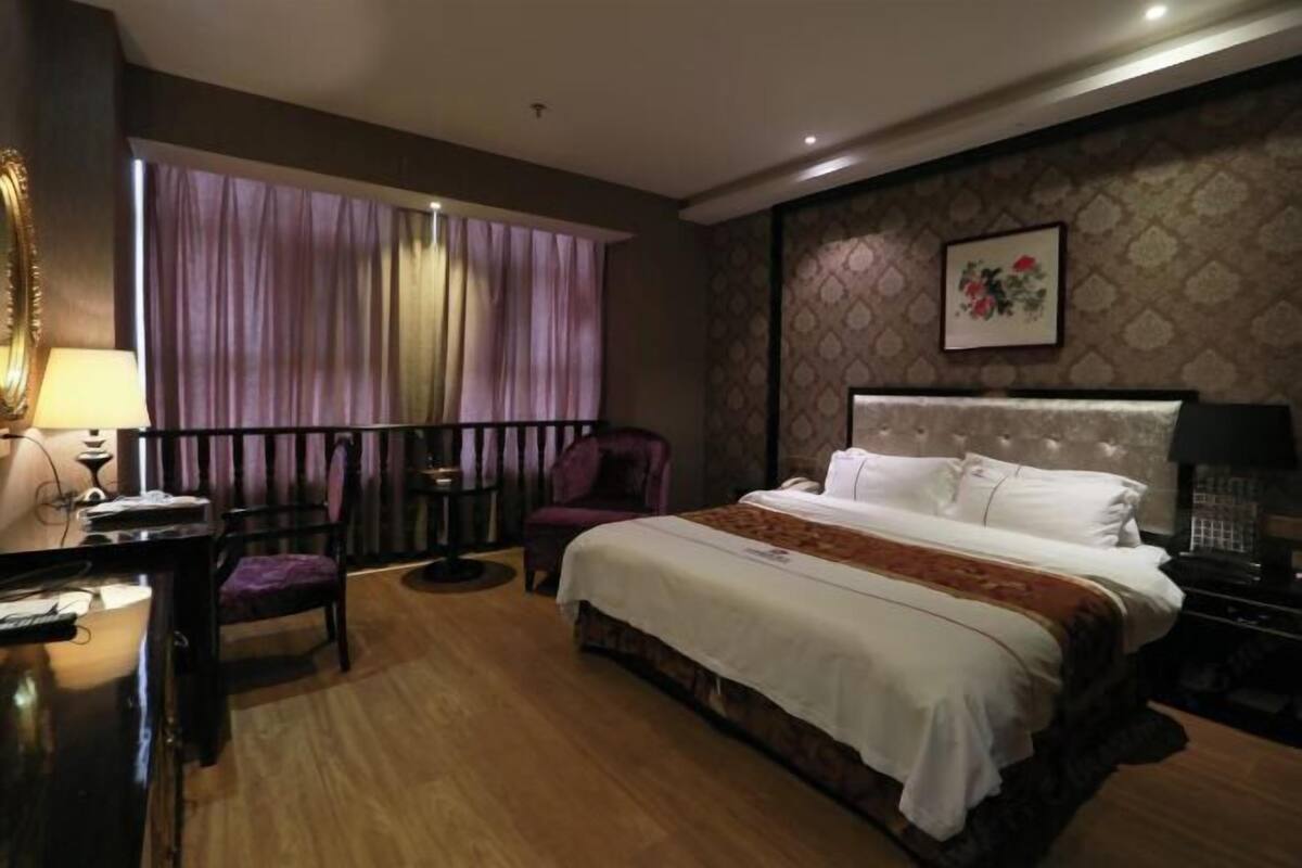 Een hotelkamer met een groot bed, een bureau met een stoel, een klein tafeltje, een stoel, en een raam met gordijnen.