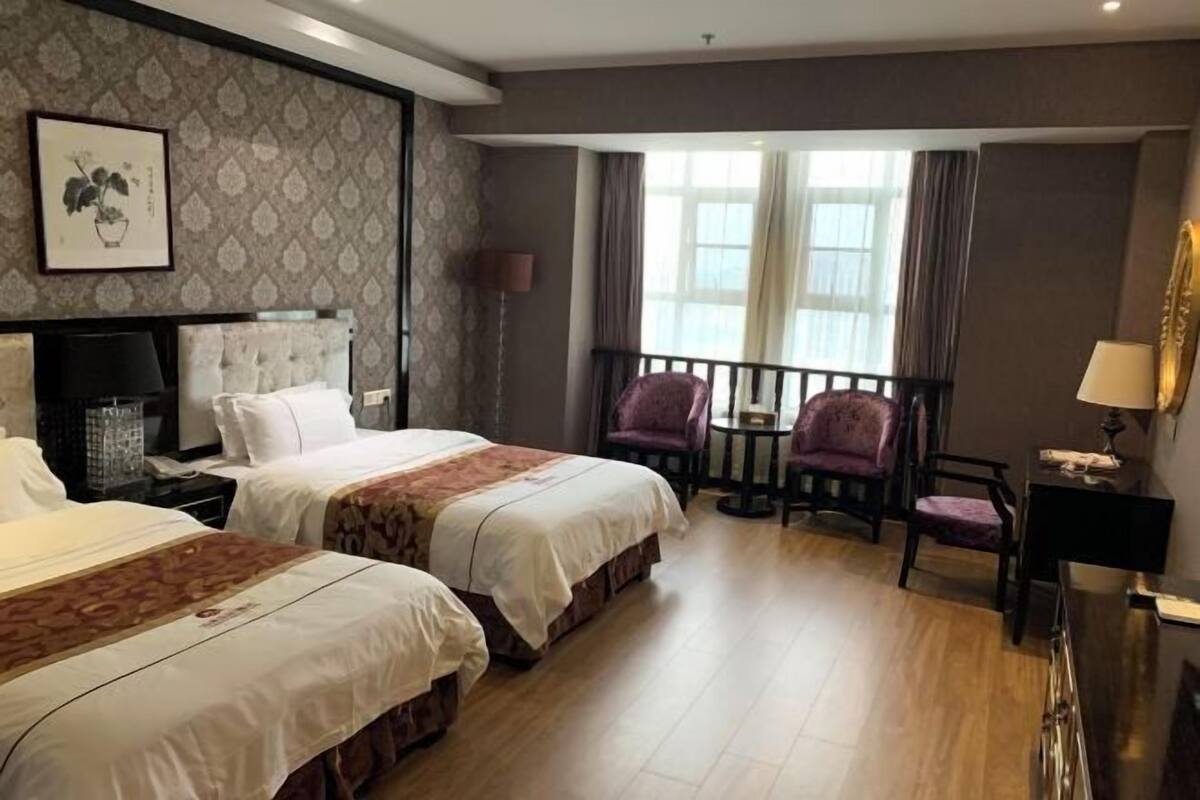 Een hotelkamer met twee bedden, een klein balkon, een bureau met lamp en een lijst aan de muur.