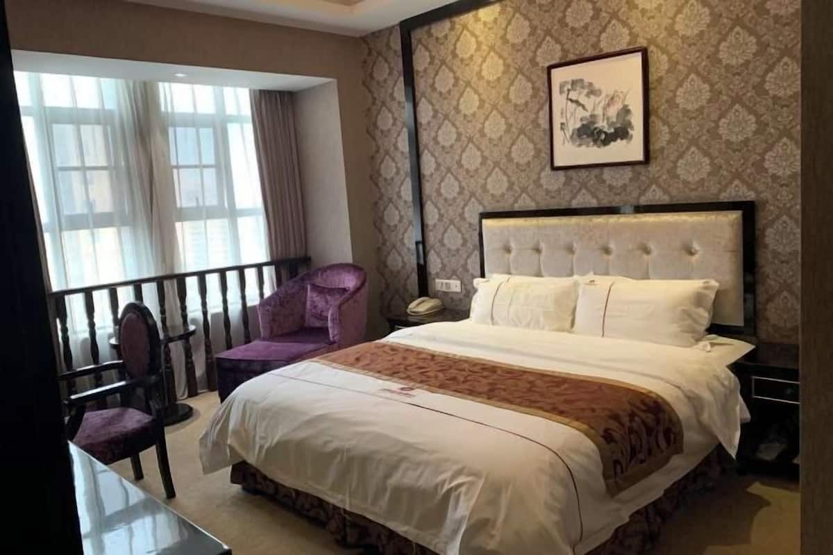 Een hotelkamer met een groot bed, een stoel, een tafel en een raam met gordijnen.