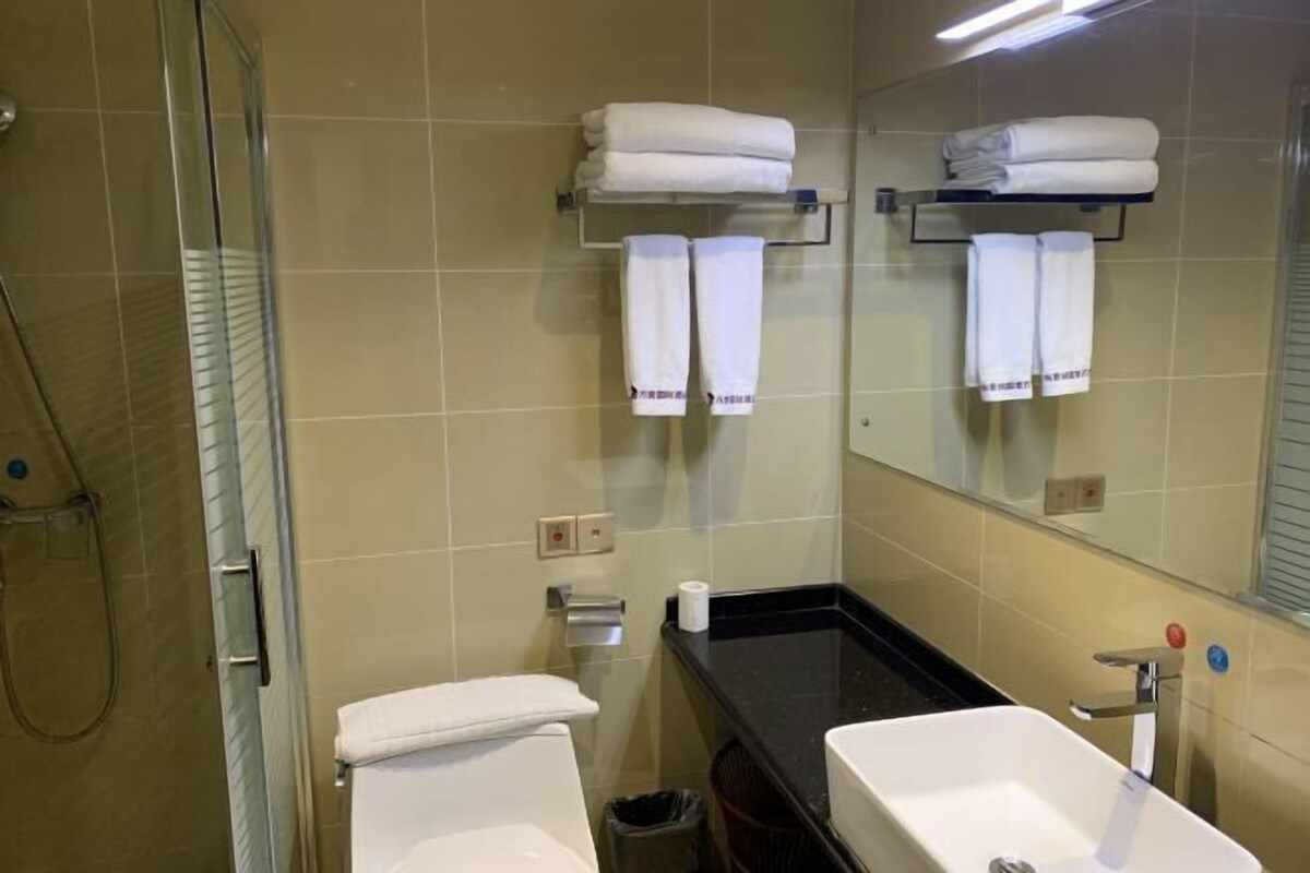 Une salle de bain avec une douche à parois de verre, des toilettes blanches, un lavabo noir et un miroir qui reflète la salle de bain.