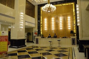 Un vestíbulo de hotel con una recepción, una araña y un suelo a cuadros.