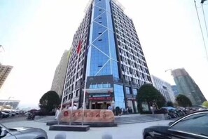 Un edificio de varios pisos con un diseño arquitectónico moderno, que presenta una entrada destacada con fachada de vidrio y un letrero grande.