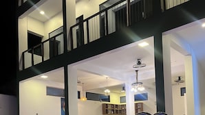 En swimmingpool med metalstige, omgivet af et spiseområde med borde og stole, og en trappe der fører op til en etage med balkon.