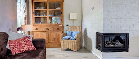 Una sala de estar con chimenea, un aparador de madera, un sillón de mimbre y un sofá de cuero marrón.