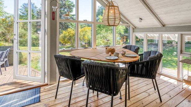 A covered patio with a wooden table and chairs, large windows, and hanging lights. - "Palle" - 400m from the sea by Interhome (Ebeltoft)