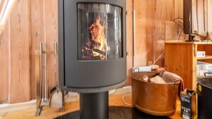A wood-burning stove with visible flames, a metal spoon rack, a copper pot with logs, and a black kettle on a wooden table. - "Palle" - 400m from the sea by Interhome (Ebeltoft)