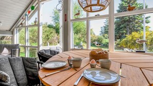 A wooden table with plates, cups, and cutlery, set in a room with large windows and a view of greenery outside. - "Palle" - 400m from the sea by Interhome (Ebeltoft)