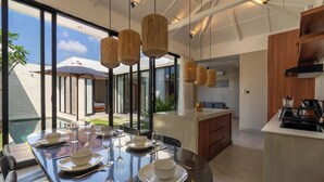 Una cocina moderna con una isla central, ventanas amplias y un comedor con mesa y sillas de vidrio.