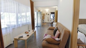 Una sala de estar con un sofá, una mesa de centro y un televisor. Se observa una cocina al fondo.