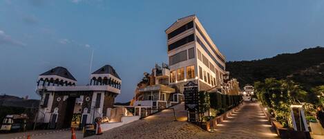 A hotel with a modern design, featuring a prominent staircase leading to the entrance, a well-lit pathway, and a view of the surrounding landscape.