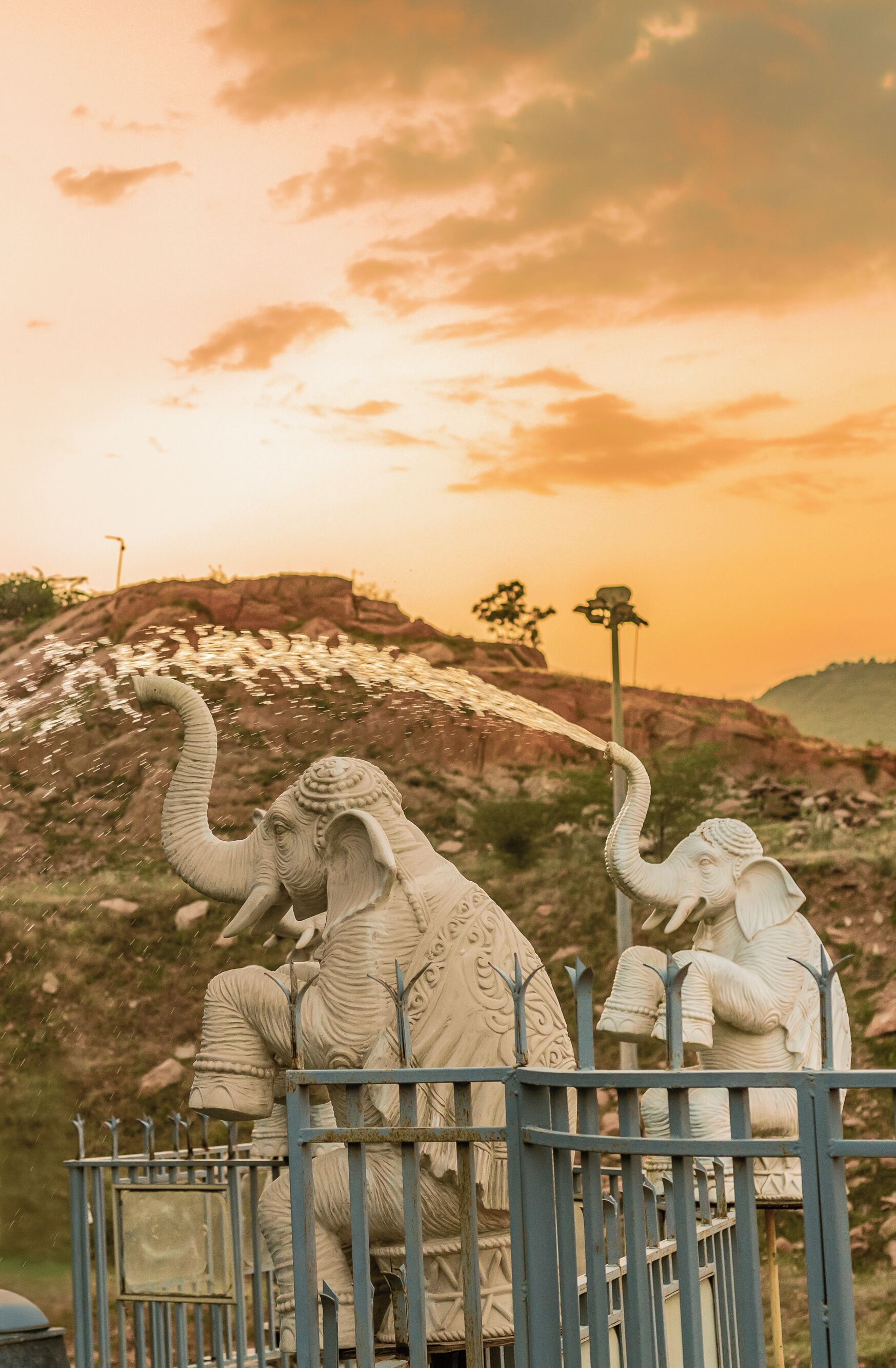 A statue of an elephant with intricate carvings, set against a backdrop of a sunset and rocky terrain.