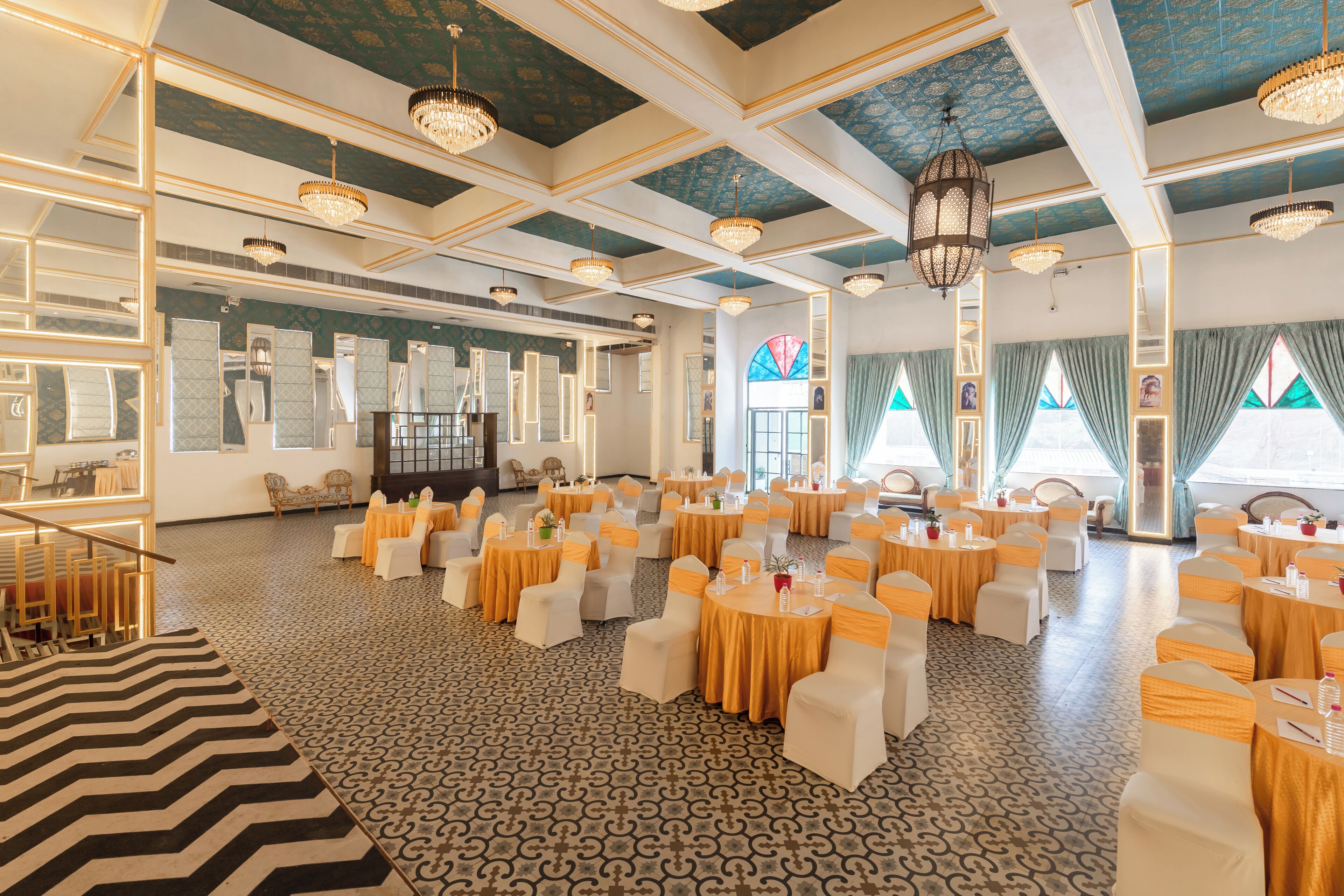 Un amplio salón de banquetes con mesas redondas y sillas blancas, un suelo con diseño y candelabros.