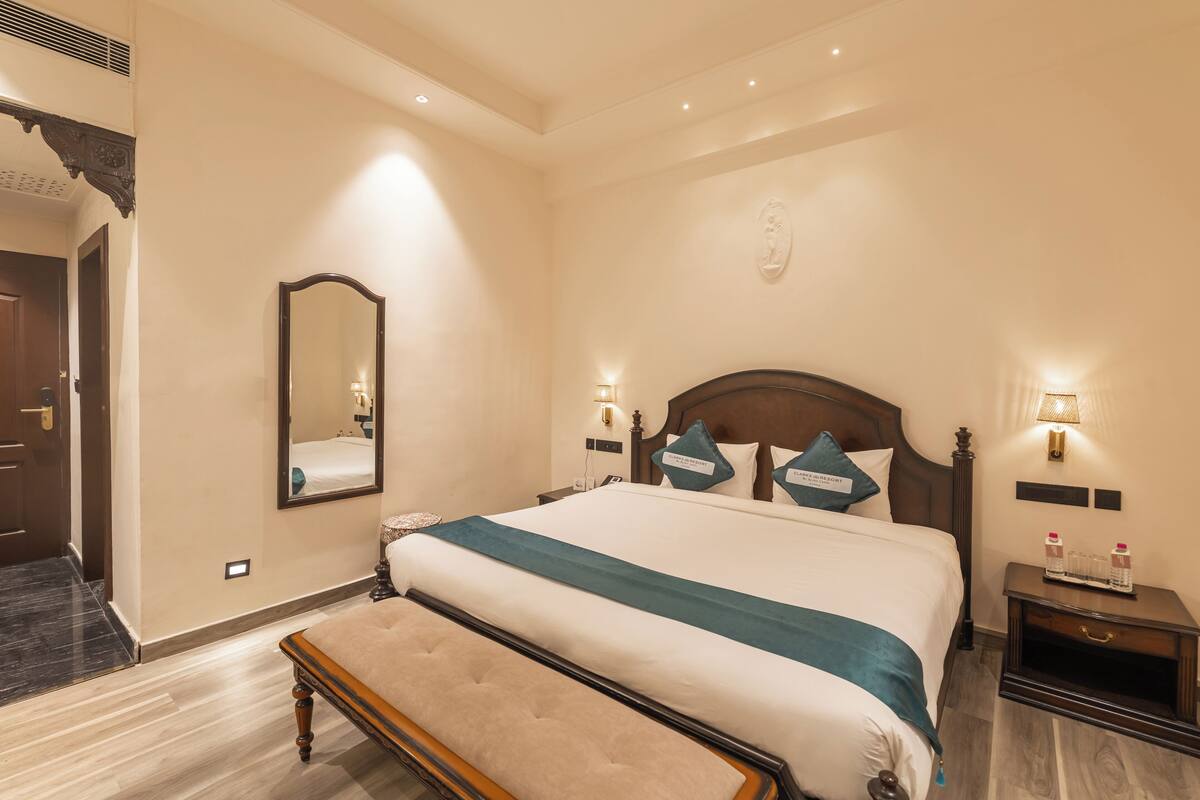 A hotel room with a large bed, a bench, a nightstand, and a wall-mounted mirror.