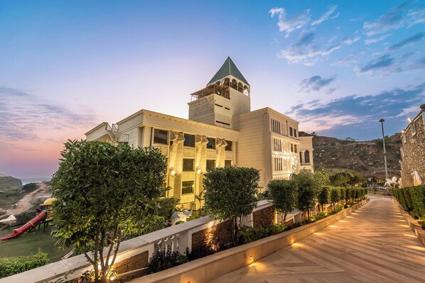 A hotel with a prominent tower, a well-lit pathway, and a view of a beach.