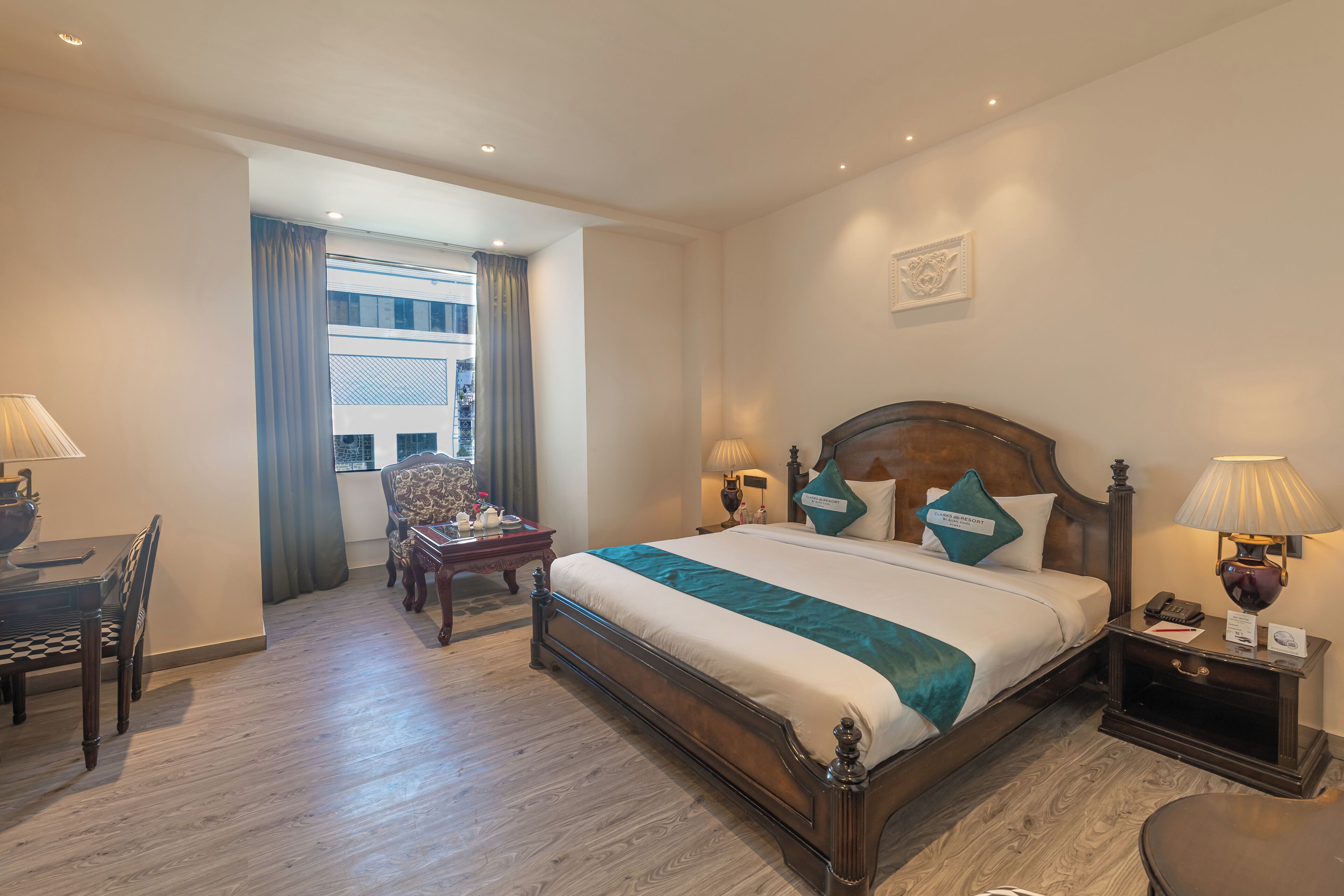 Quarto de hotel com uma cama grande, mesas de cabeceira, escrivaninha e uma cadeira.