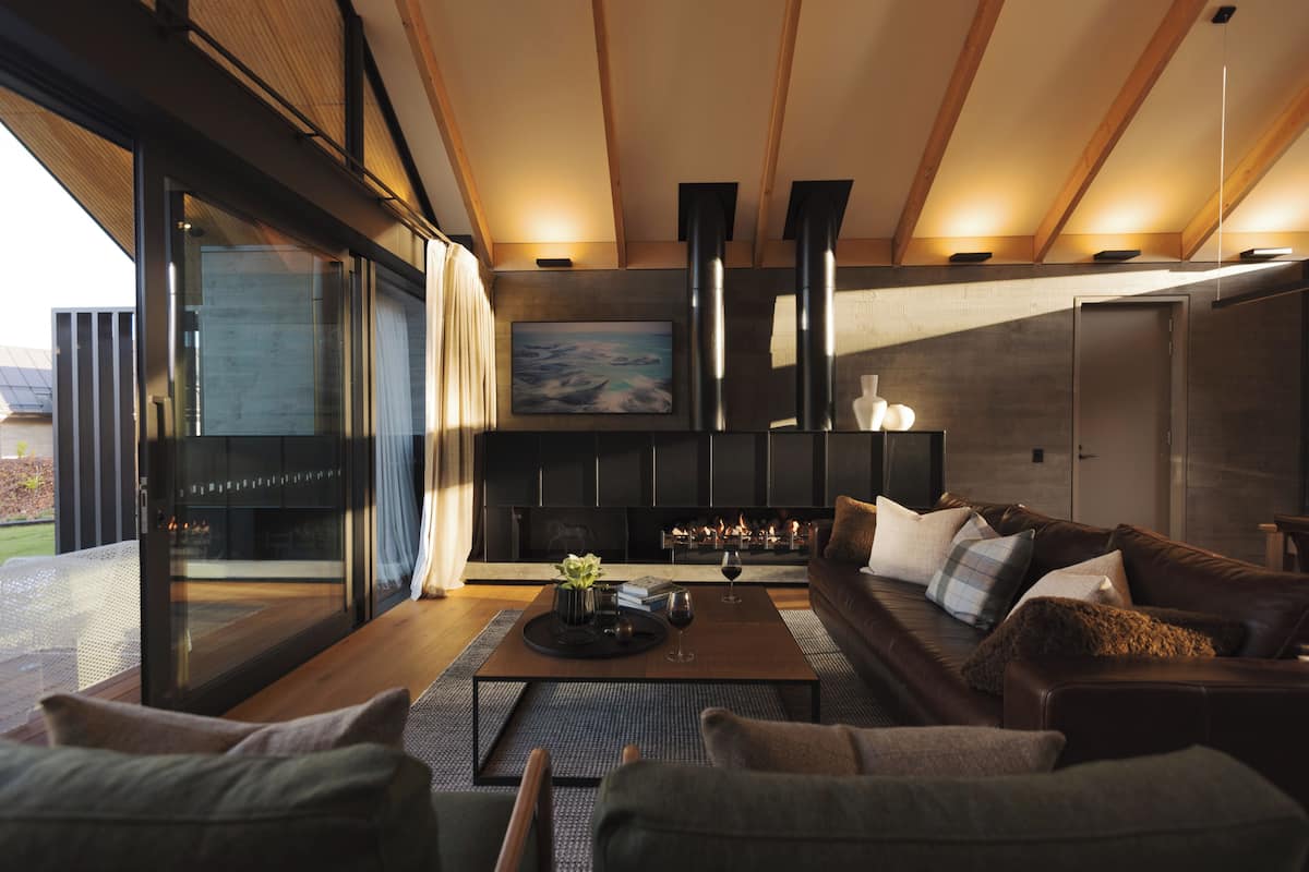A modern living room with a fireplace, leather sofa, and a glass door leading to an outdoor area.