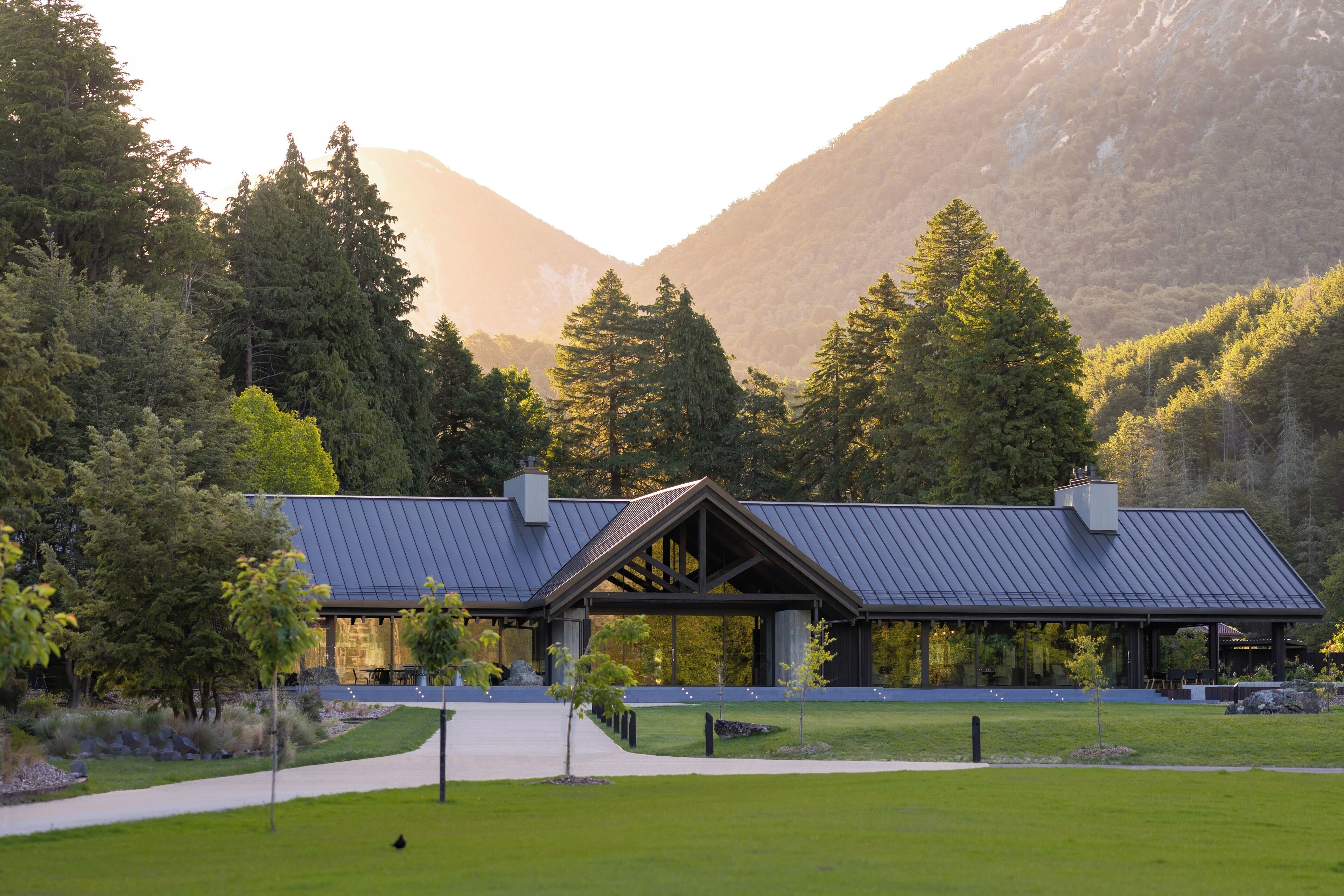 A modern building with a sloped roof, surrounded by lush greenery and mountains in the background.