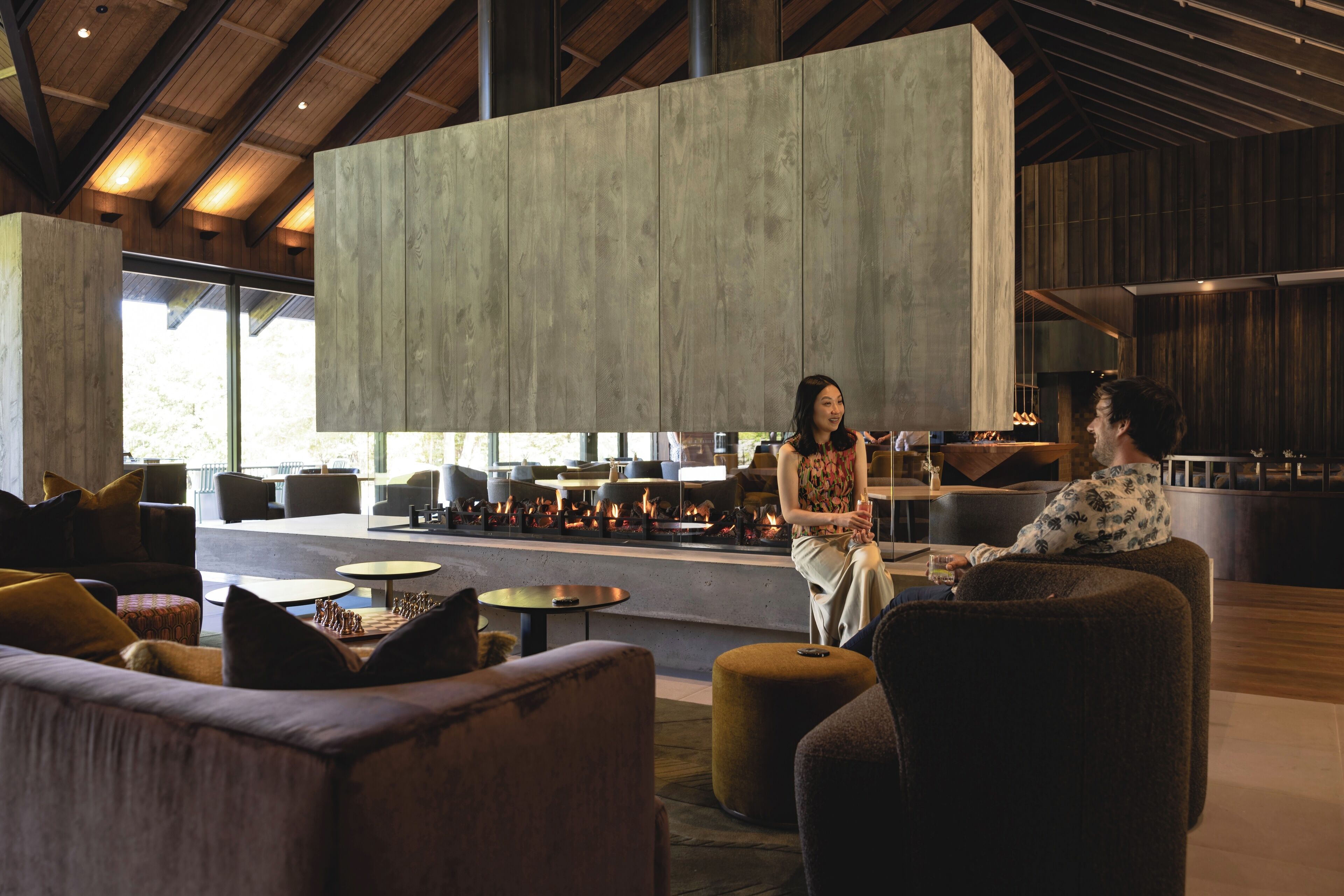 Een moderne zithoek met comfortabele zitplaatsen, een open haard en een groot raam met uitzicht op de omgeving.