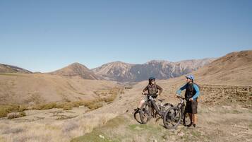 Dos personas en un sendero de bicicleta de montaña, cielo despejado y montañas a lo lejos.