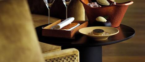 A table with a bottle of champagne, two glasses, a plate with a dessert, and a tray with a napkin and a small bowl.