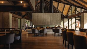 A spacious indoor area with high ceilings, wooden beams, and large windows allowing natural light. Tables and chairs are arranged for dining or meetings. - Flockhill (Lake Pearson)