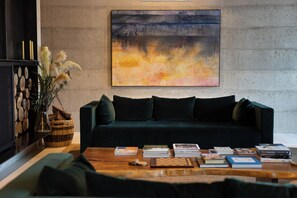 A modern living room with a dark green sofa, a wooden coffee table with books and a chess set, a large abstract painting on the wall, and a decorative plant.