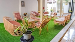 A covered outdoor seating area with wicker furniture and a green artificial turf floor. - Grand Malioboro Yogyakarta Hotel (Gedong Tengen)