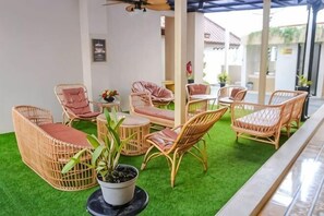 Een overdekte zitruimte met rieten meubels en een vloer van kunstgras.