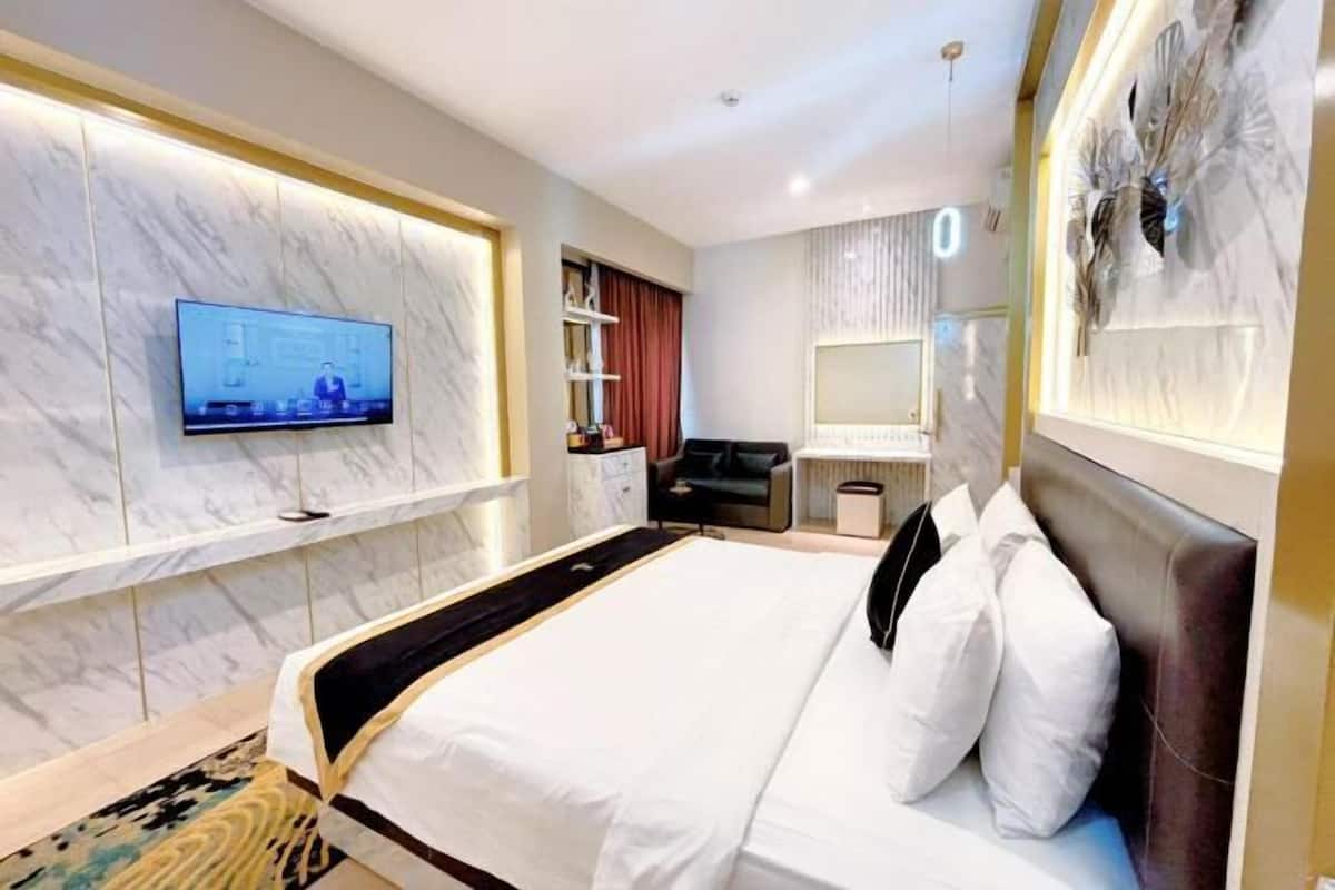 Ein modernes Hotelzimmer mit einem großen Bett, einem flachbildfernseher an der Wand, einem Schminktisch mit Spiegel und einer dekorativen Wandverkleidung.