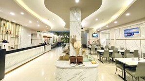 A modern hotel lobby with a marble reception desk, seating area, and a central column with decorative items. - Grand Malioboro Yogyakarta Hotel (Gedong Tengen)